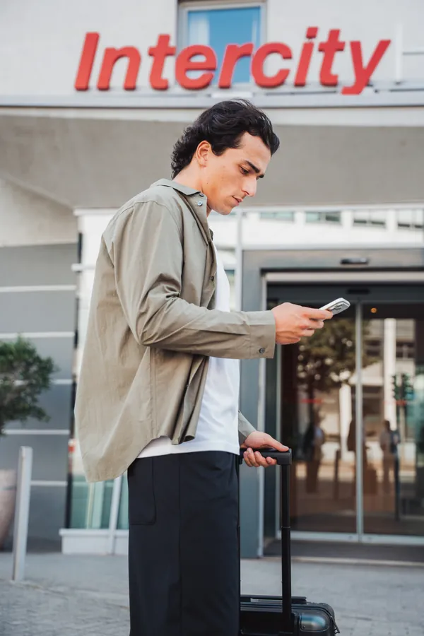 Gast mit Koffer schaut vor dem Hotel auf sein Smartphone
